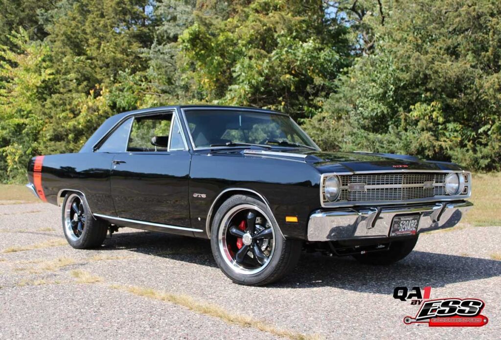 Black classic Dodge Dart GTS parked beside trees