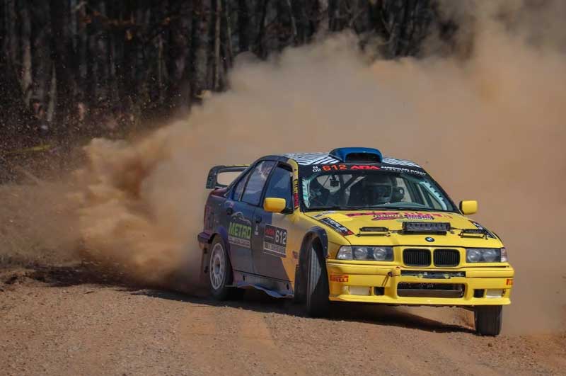 Yellow rally car racing on dirt, kicking up dust